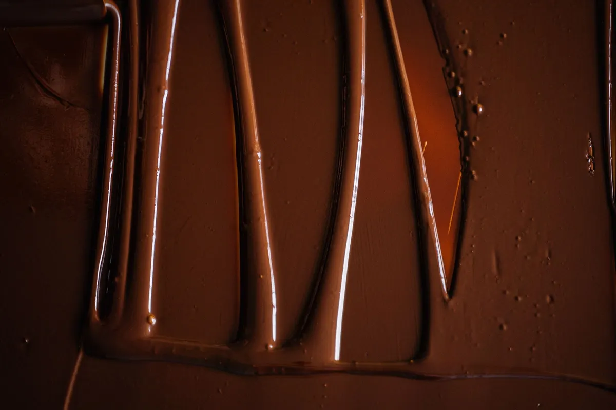 Fluid tempered chocolate spread across a bench in glossy ridges