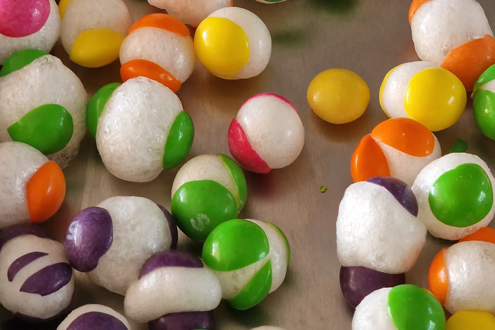 Freeze-dried shell candy on a tray, the sugar interior puffed white and porous with fragments of the original coloured shell still attached